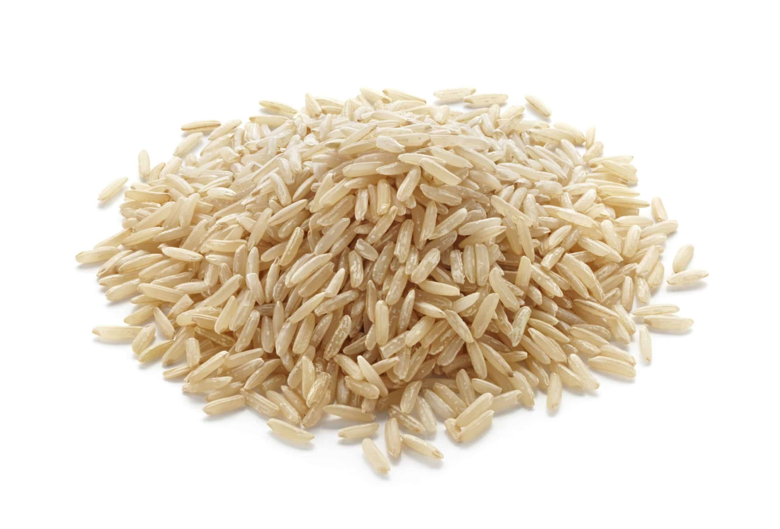 Pile of uncooked long-grain white rice scattered on a white background.