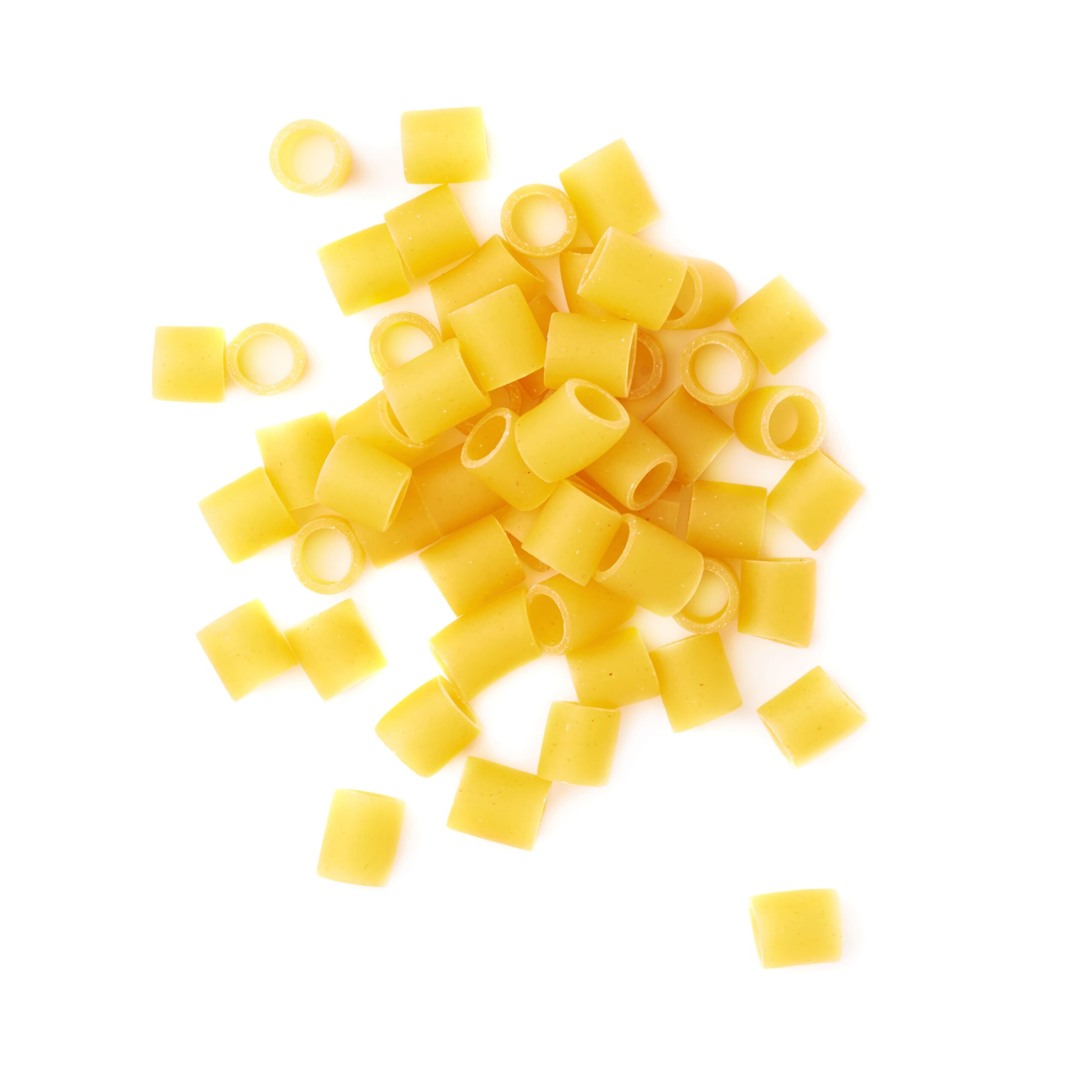 Close-up of uncooked yellow tubular pasta pieces scattered on a white background.