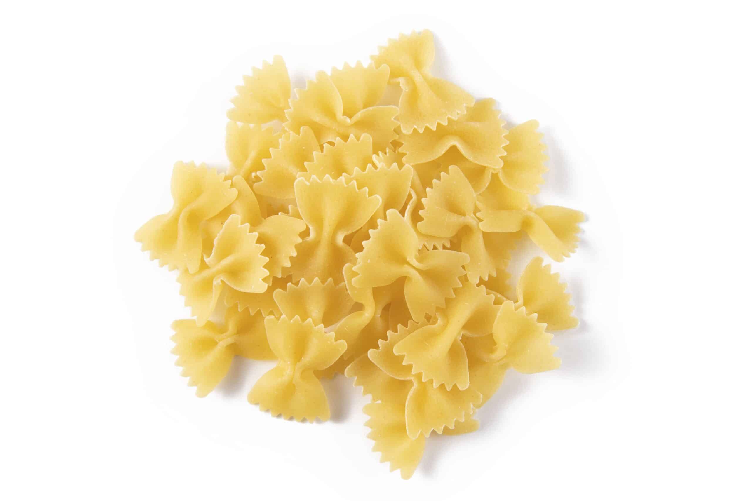 Pile of uncooked farfalle (bow-tie) pasta on a white background, light and yellow in color