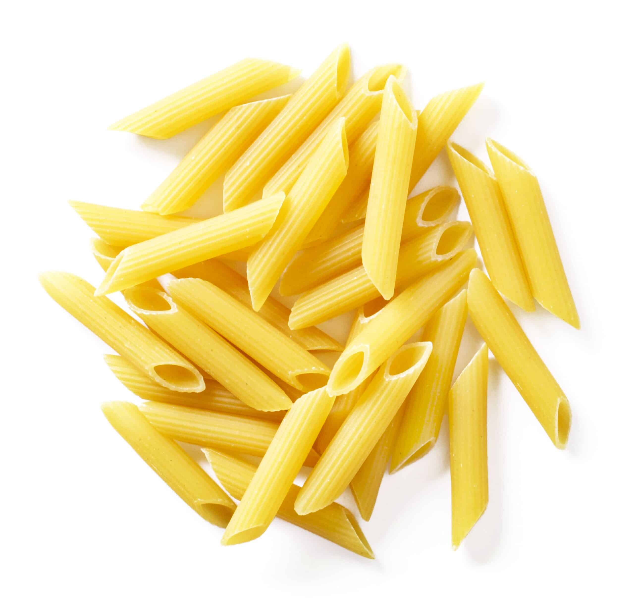 Uncooked penne pasta scattered on a white background
