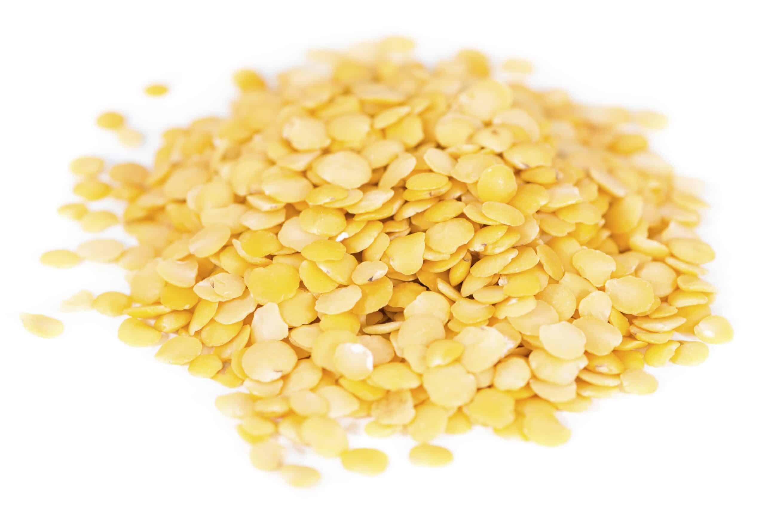 Pile of yellow split lentils on a white background, uncooked and dry.